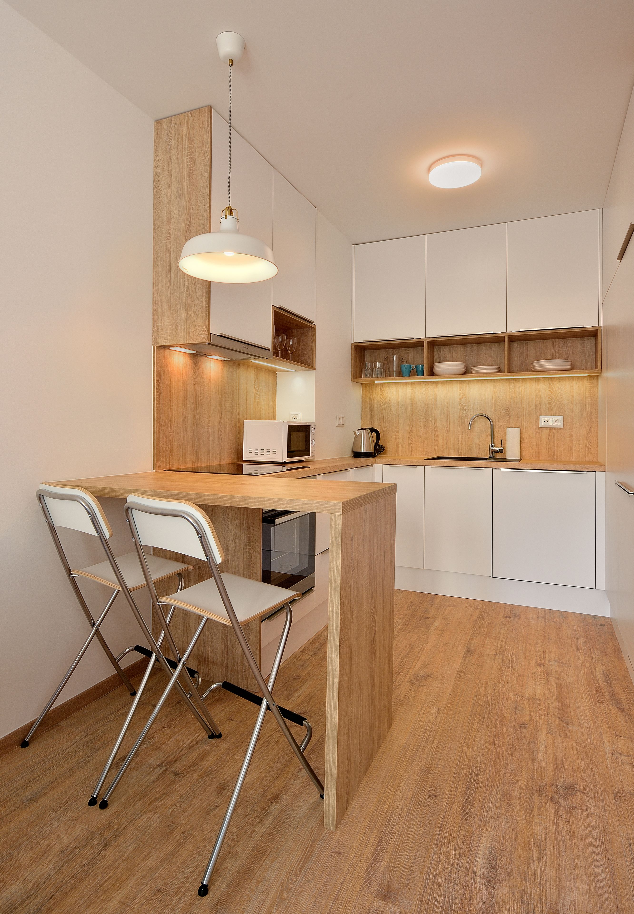 A modern kitchen with a wooden island, white bar stools, a built-in microwave, and a sink.