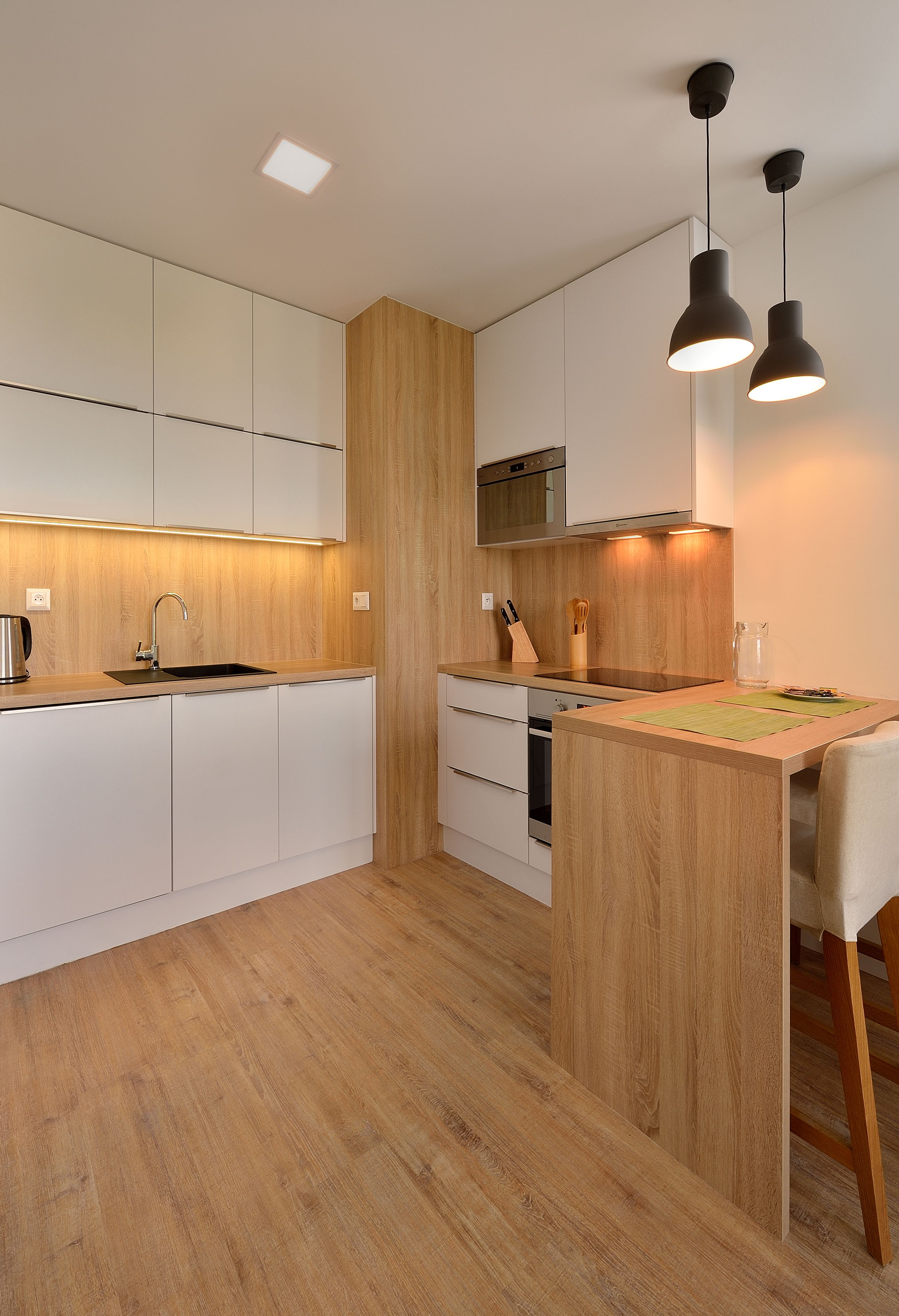 Una cocina moderna con armarios blancos, una isla de madera e iluminación colgante.