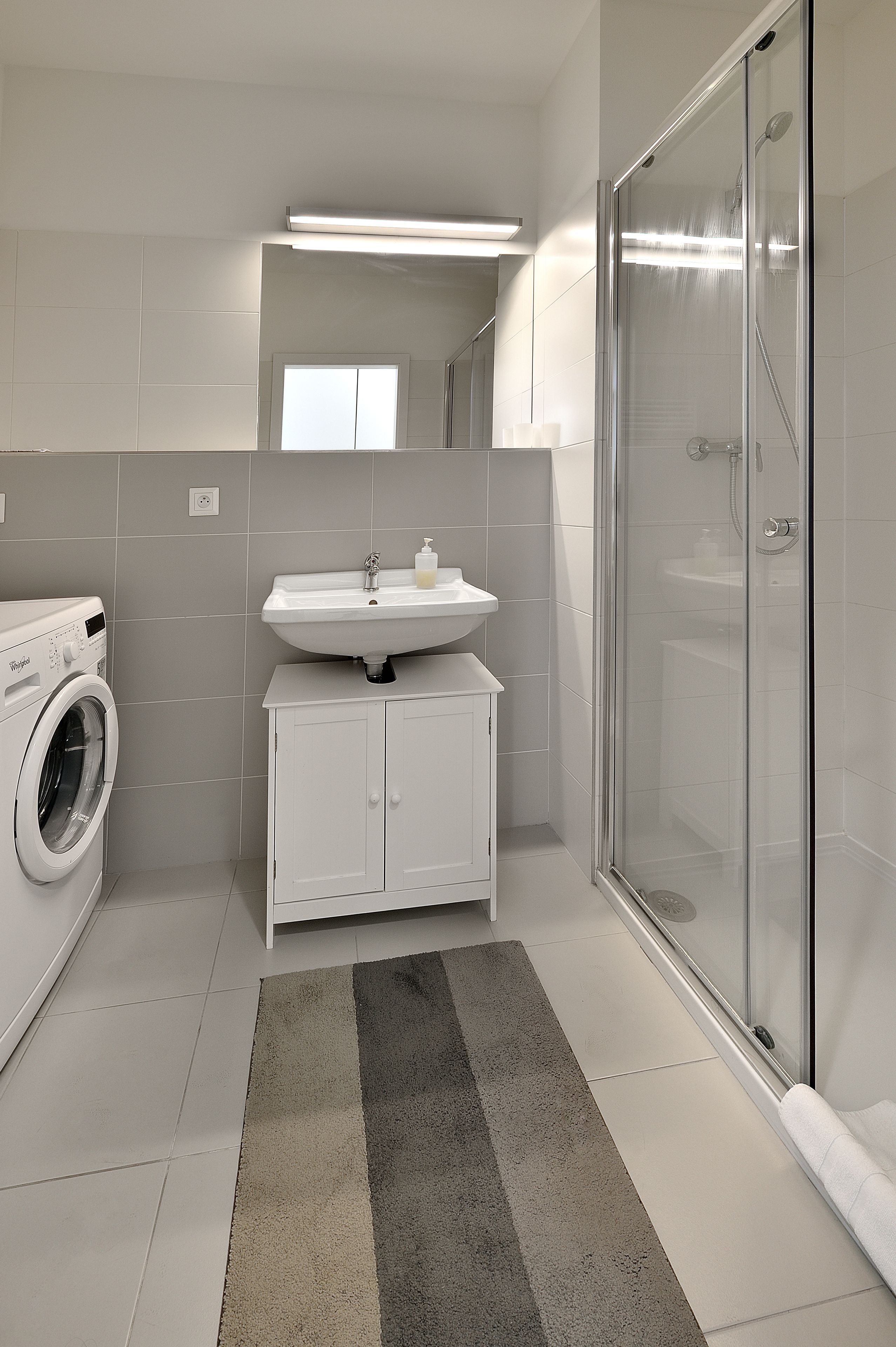 Une salle de bain moderne équipée d’un lave-linge, d’un lavabo et d’une douche à parois de verre.