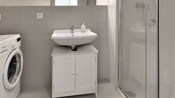 Une salle de bain moderne équipée d’un lave-linge, d’un lavabo et d’une douche à parois de verre.