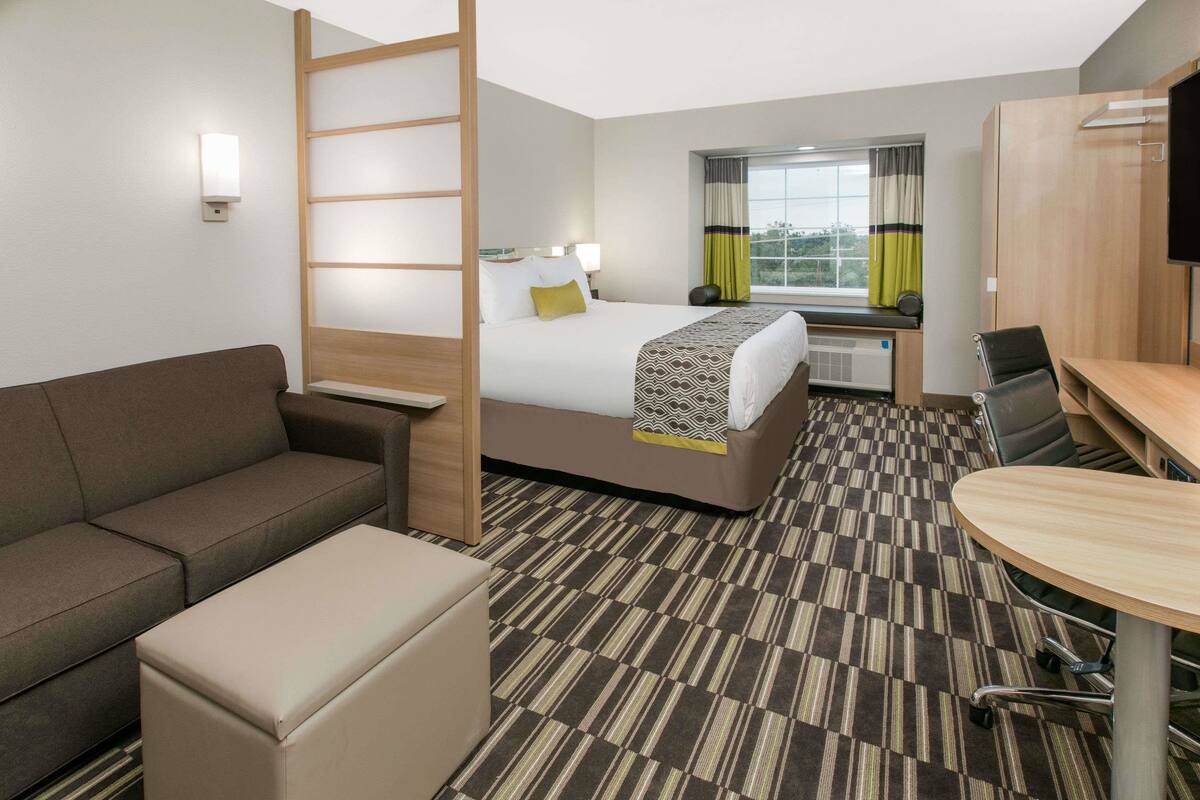 A hotel room with a bed, a sofa, a small table, and a TV.