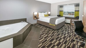 A hotel room with a large bed, a separate bathroom with a bathtub, a desk, and a window with curtains. - Microtel Inn & Suites by Wyndham Lubbock (Lubbock)