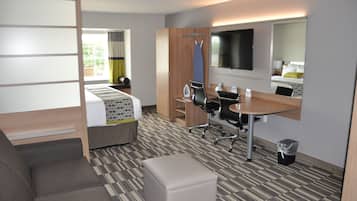 Habitación de hotel moderna con cama, escritorio, silla, mesita, cubo de basura y un espejo grande.