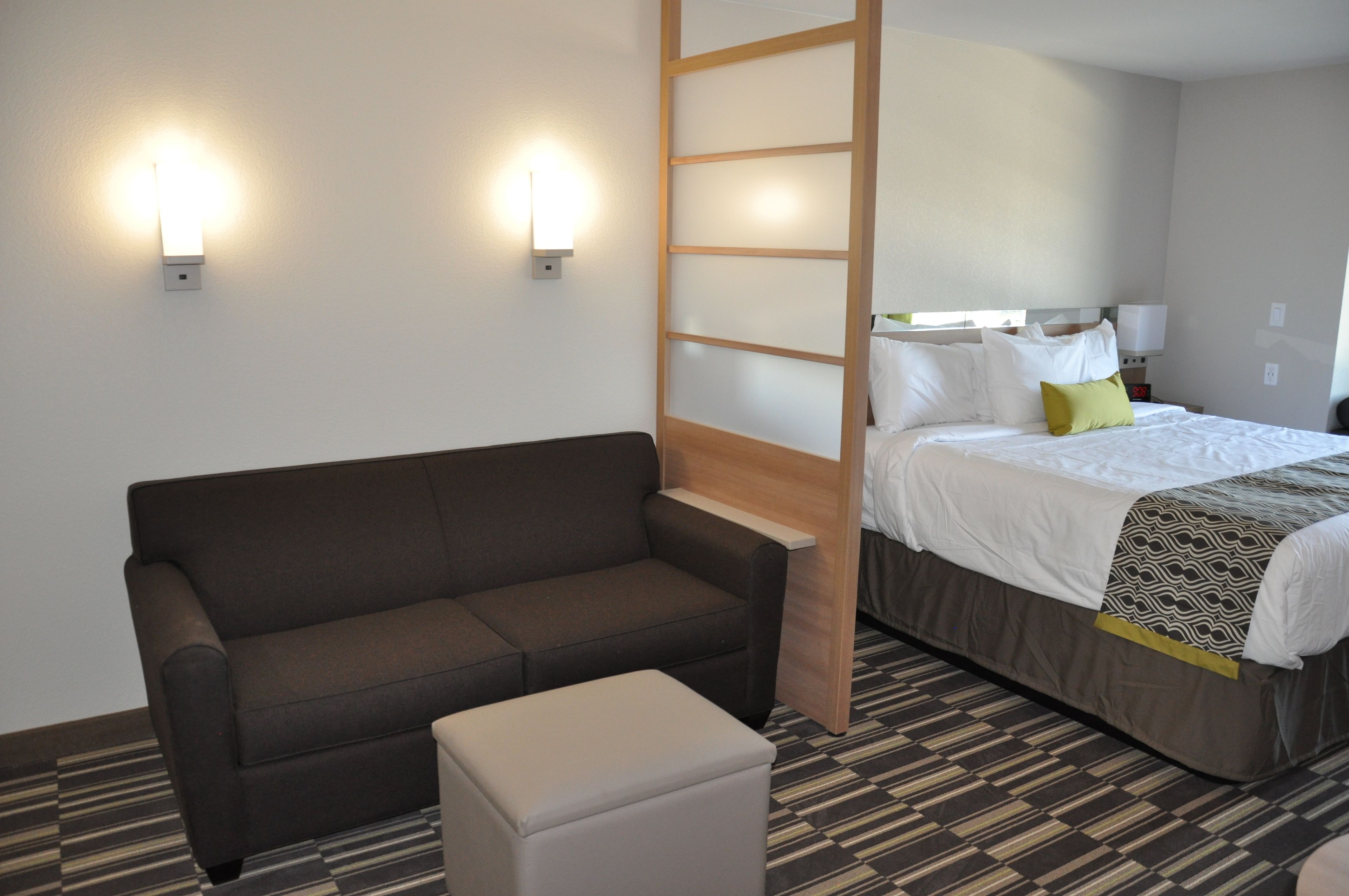 Une chambre d’hôtel avec un canapé, un lit recouvert d’une couvre-lit à motifs et deux lampes fixées au mur.