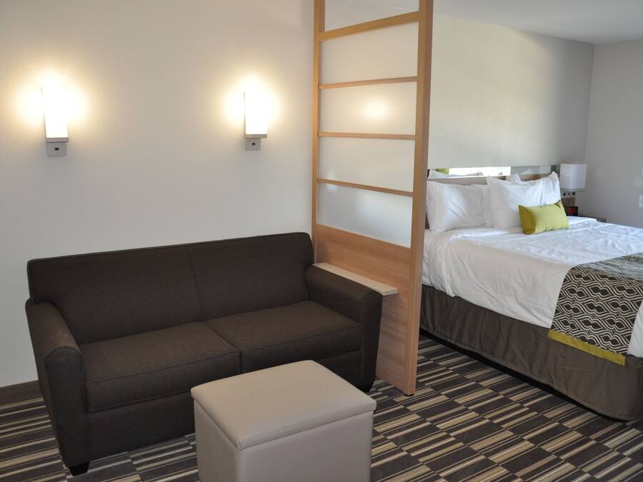 Ett hotellrum med en soffa, en säng med ett mönstrat överkast och två väggmonterade lampor.