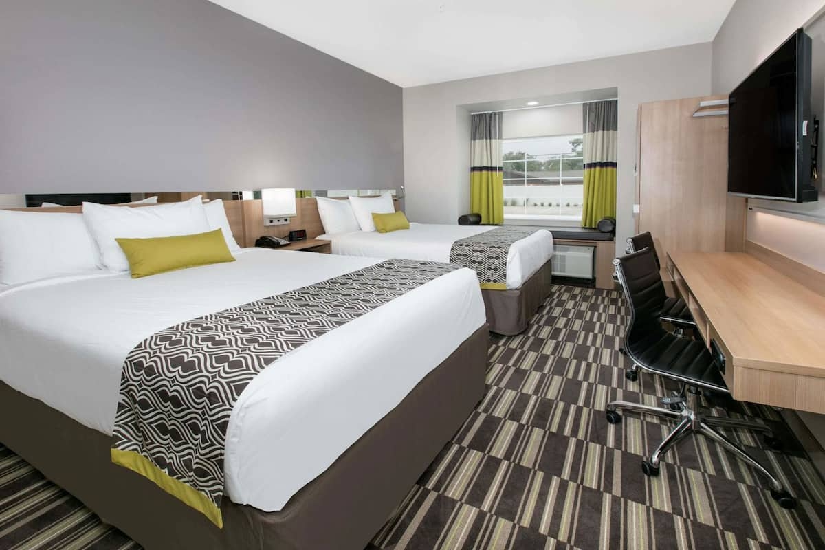 A hotel room with two beds, a desk, a chair, a TV, and a window with curtains.