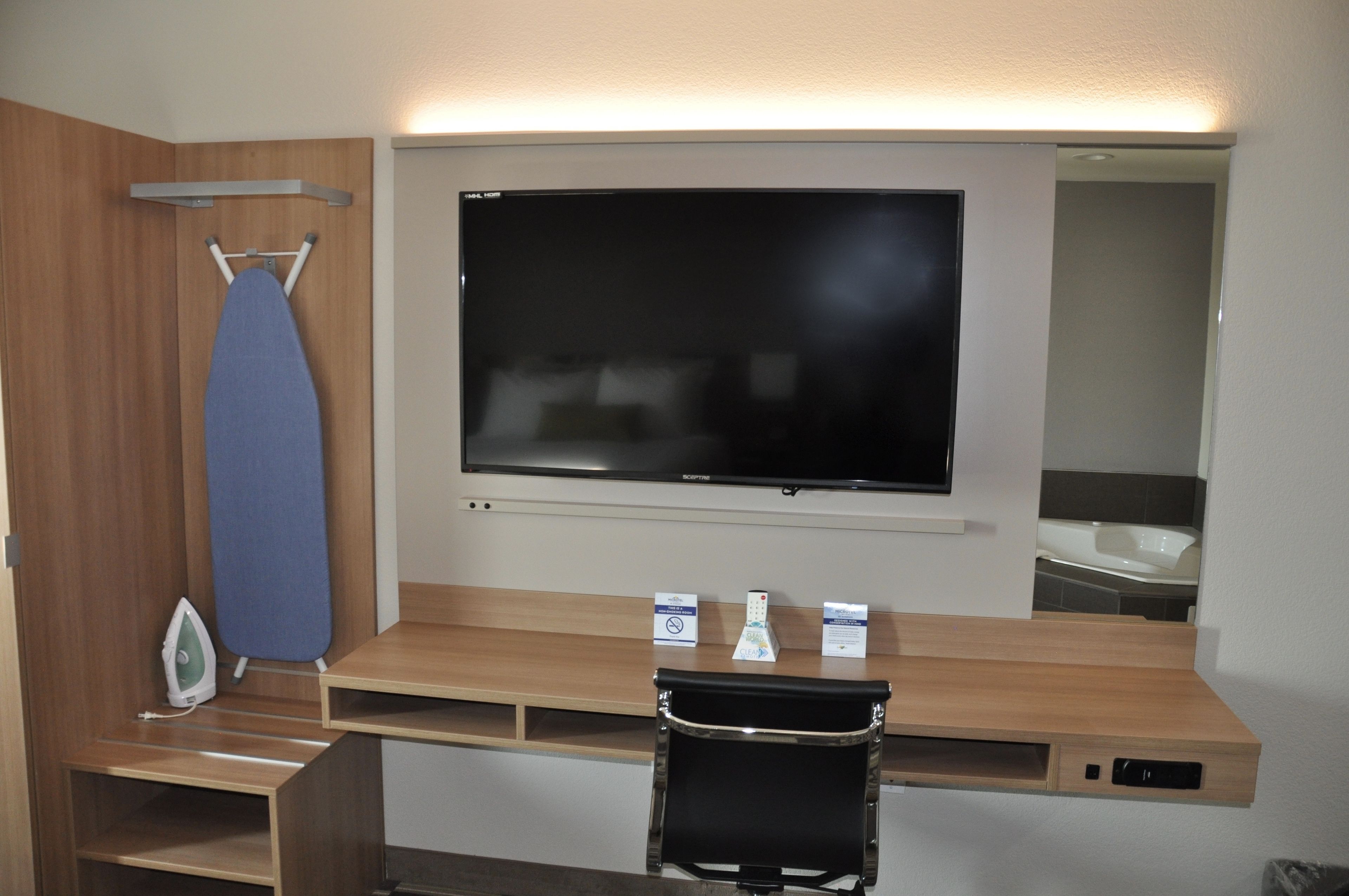 Een hotelkamer met een flatscreentelevisie, een strijkplank en een klein bureau met een stoel.