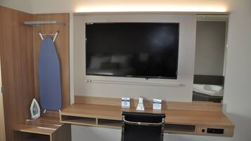 Een hotelkamer met een flatscreentelevisie, een strijkplank en een klein bureau met een stoel.
