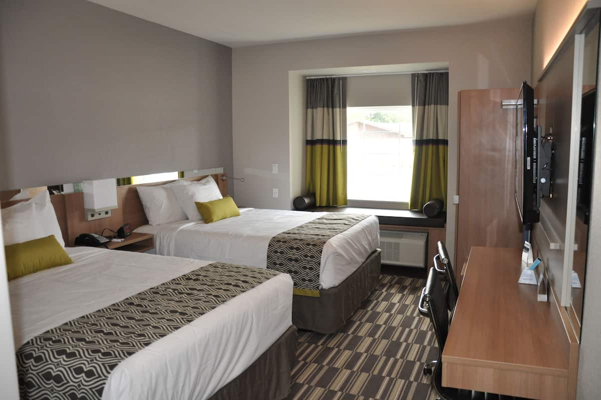 A hotel room with two beds, a desk, a TV, and a window with curtains.