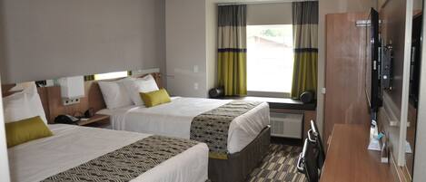 A hotel room with two beds, a desk, a TV, and a window with curtains.