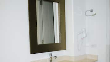 A bathroom with a white vanity, a beige countertop, a large mirror with a dark frame, a towel rack, and a wall-mounted hairdryer.