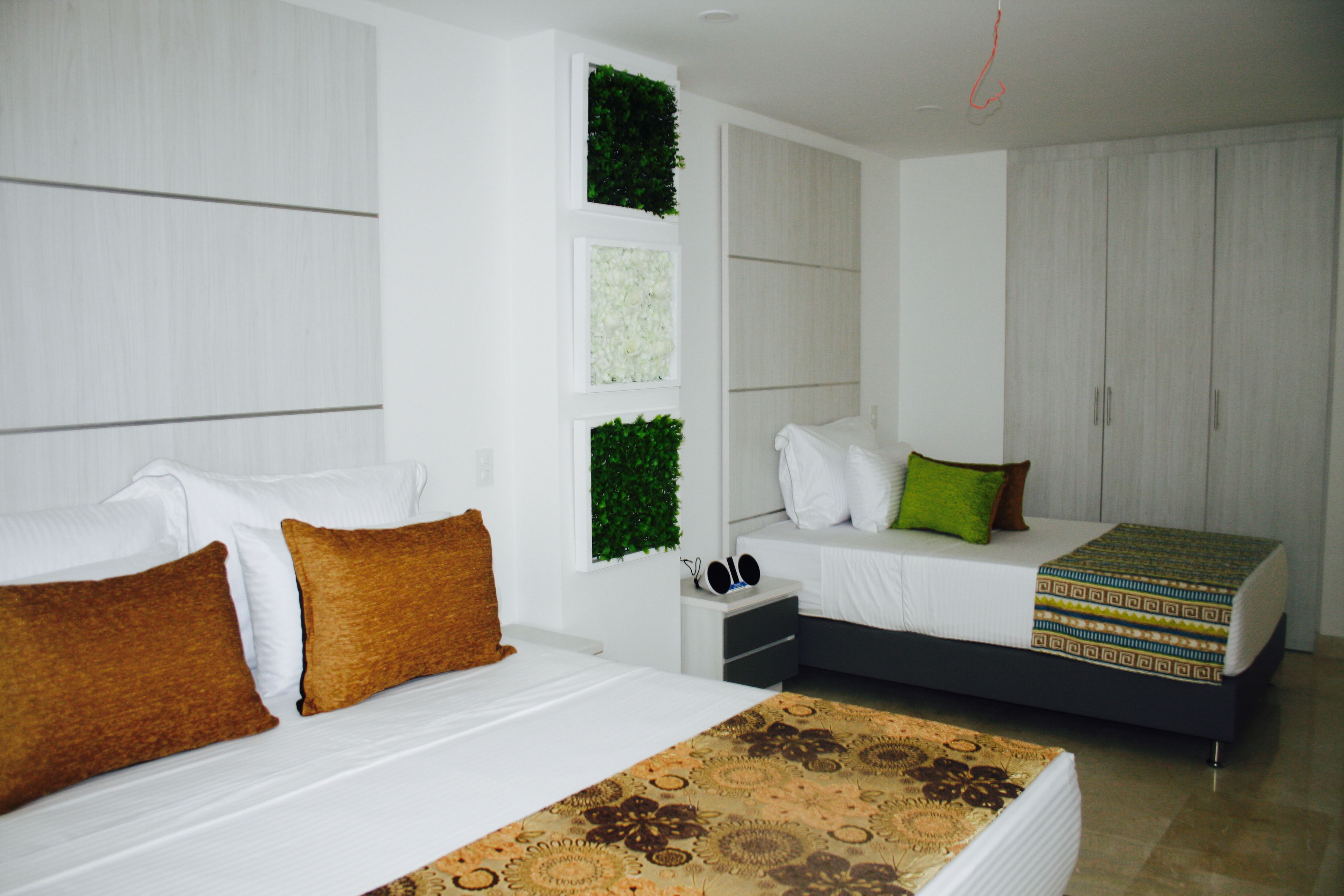 A modern bedroom with two beds, a small bedside table, and a wall-mounted shelf with greenery.