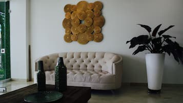 A living room with a tufted sofa, a decorative wall piece, a large potted plant, and a wooden coffee table.