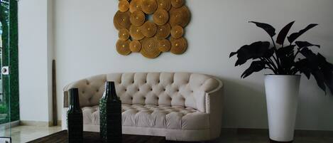 A living room with a tufted sofa, a decorative wall piece, a large potted plant, and a wooden coffee table.