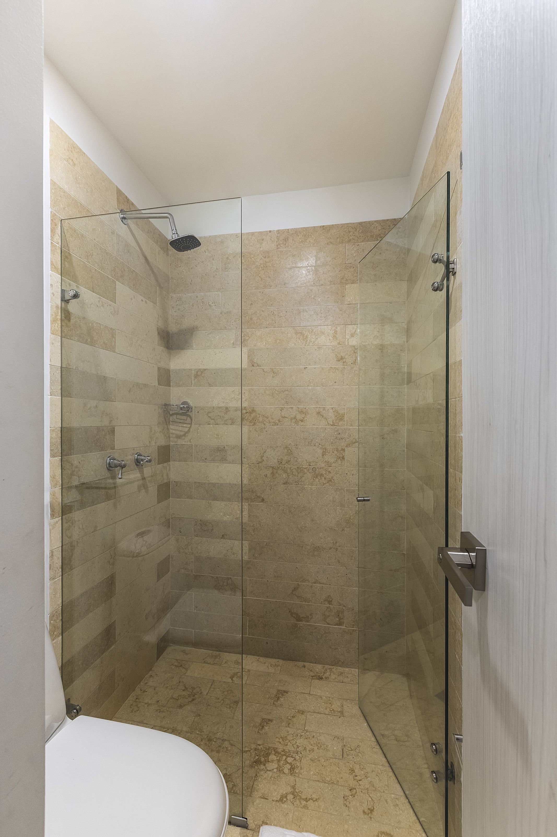 A modern bathroom with a glass-enclosed shower, beige tiles, and a white toilet.