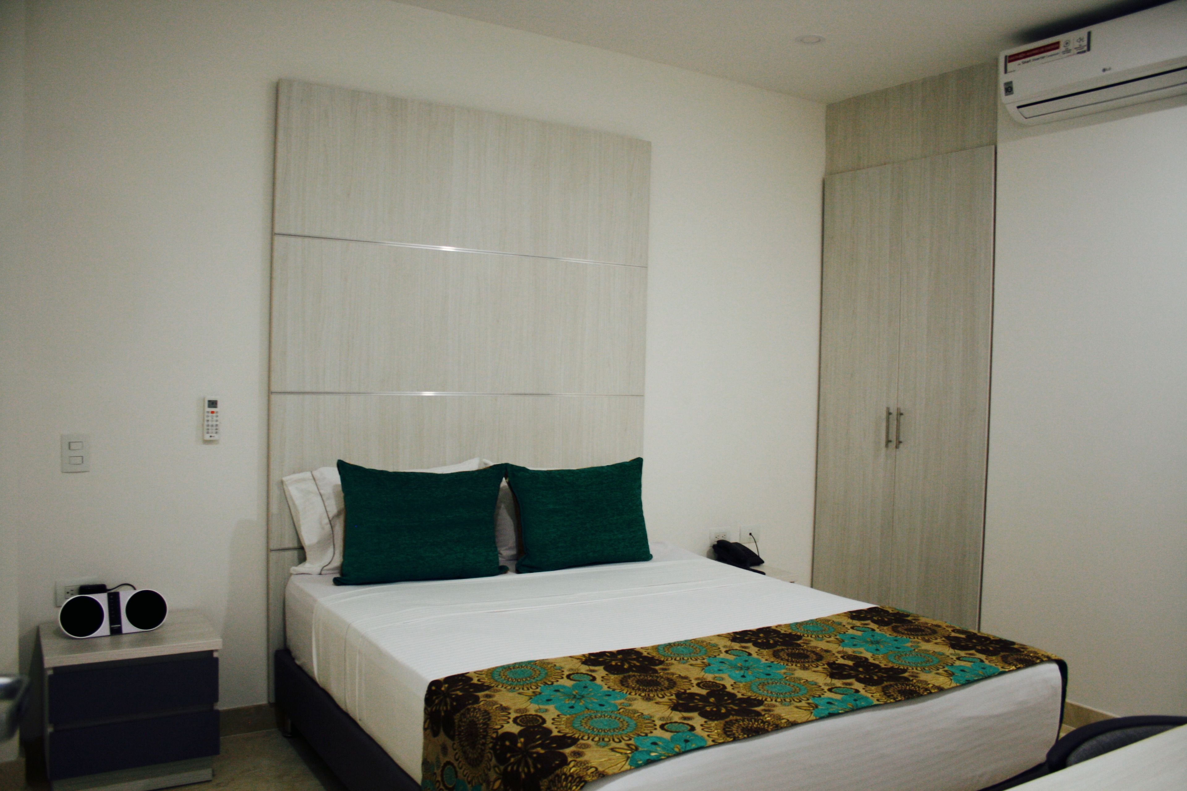 A hotel room with a bed, a nightstand, a wardrobe, and an air conditioning unit.