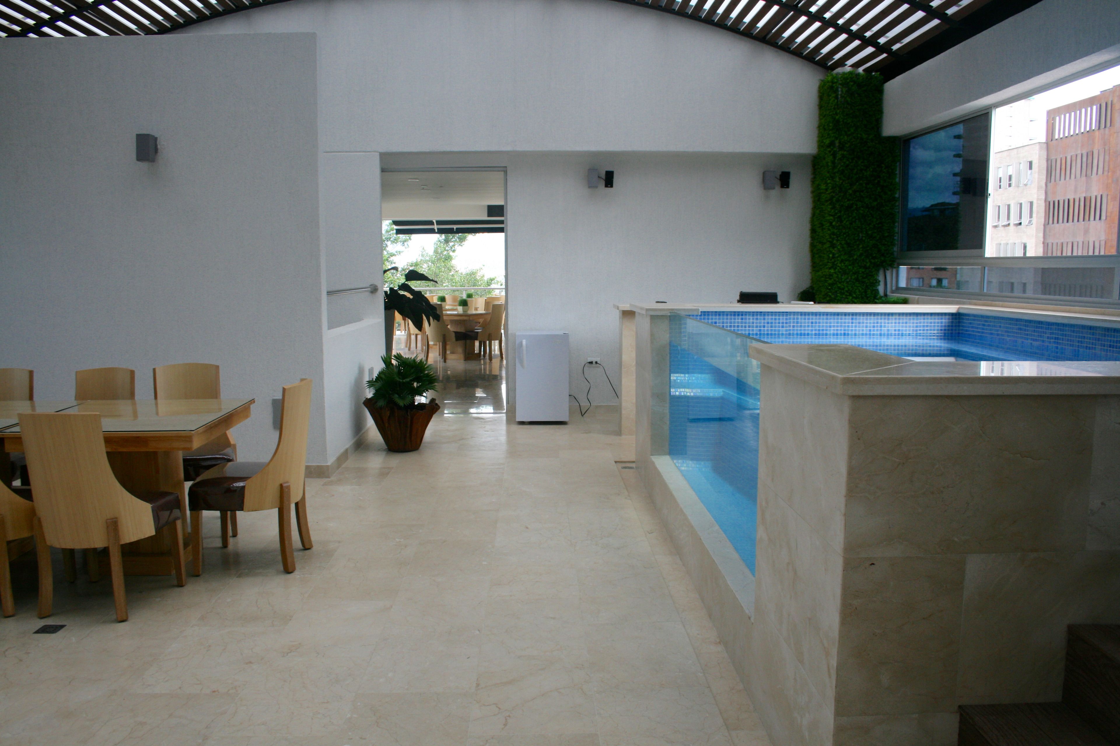 A modern indoor pool area with a clear view of the pool, a dining area with wooden chairs and a table, and a potted plant.