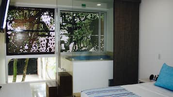A modern hotel room with a large window, a bed with a striped bedspread, a small bedside table, and a blue pillow.