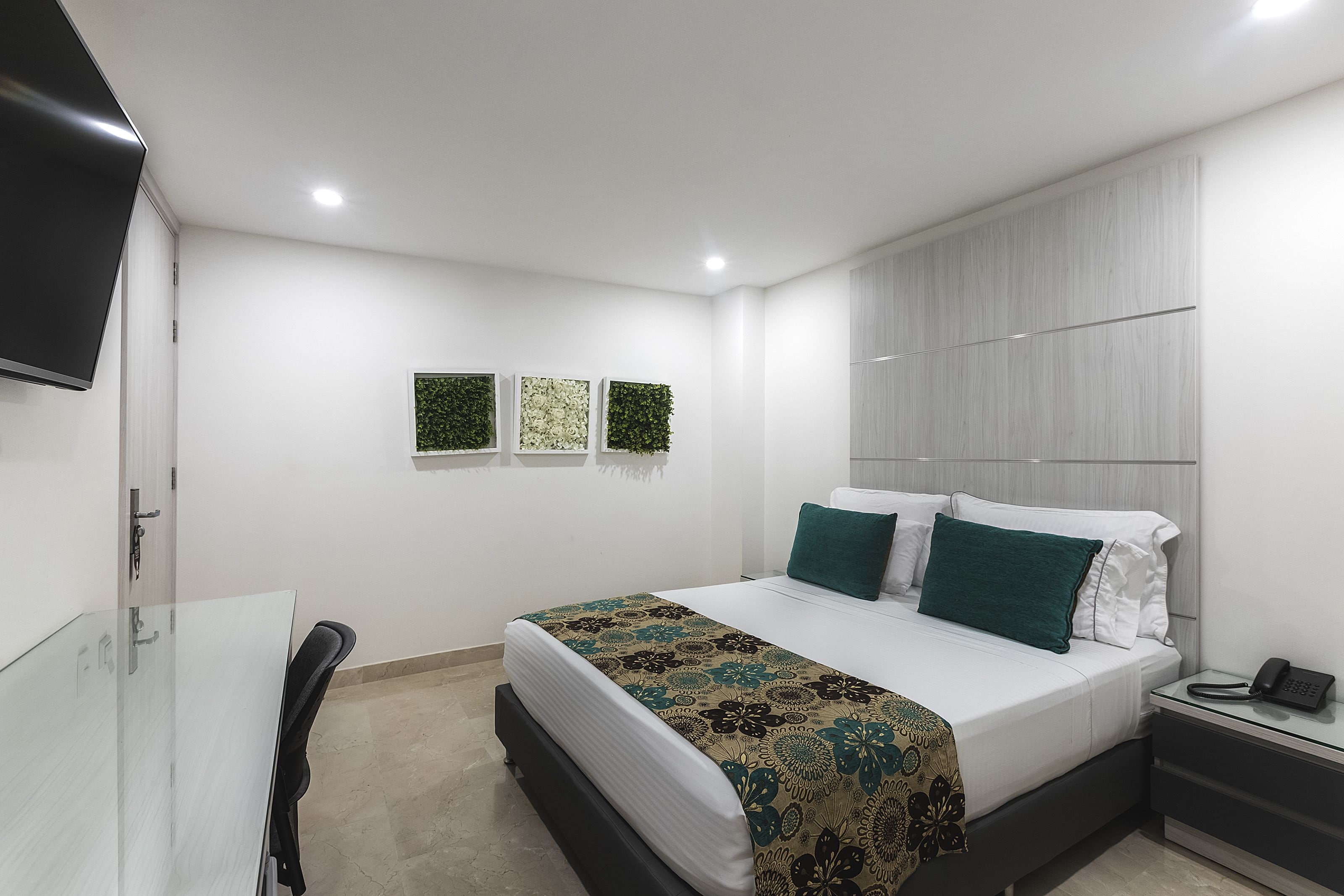 Ein modernes Hotelzimmer mit Bett, Nachttisch und einem an der Wand befestigten Flachbildfernseher.