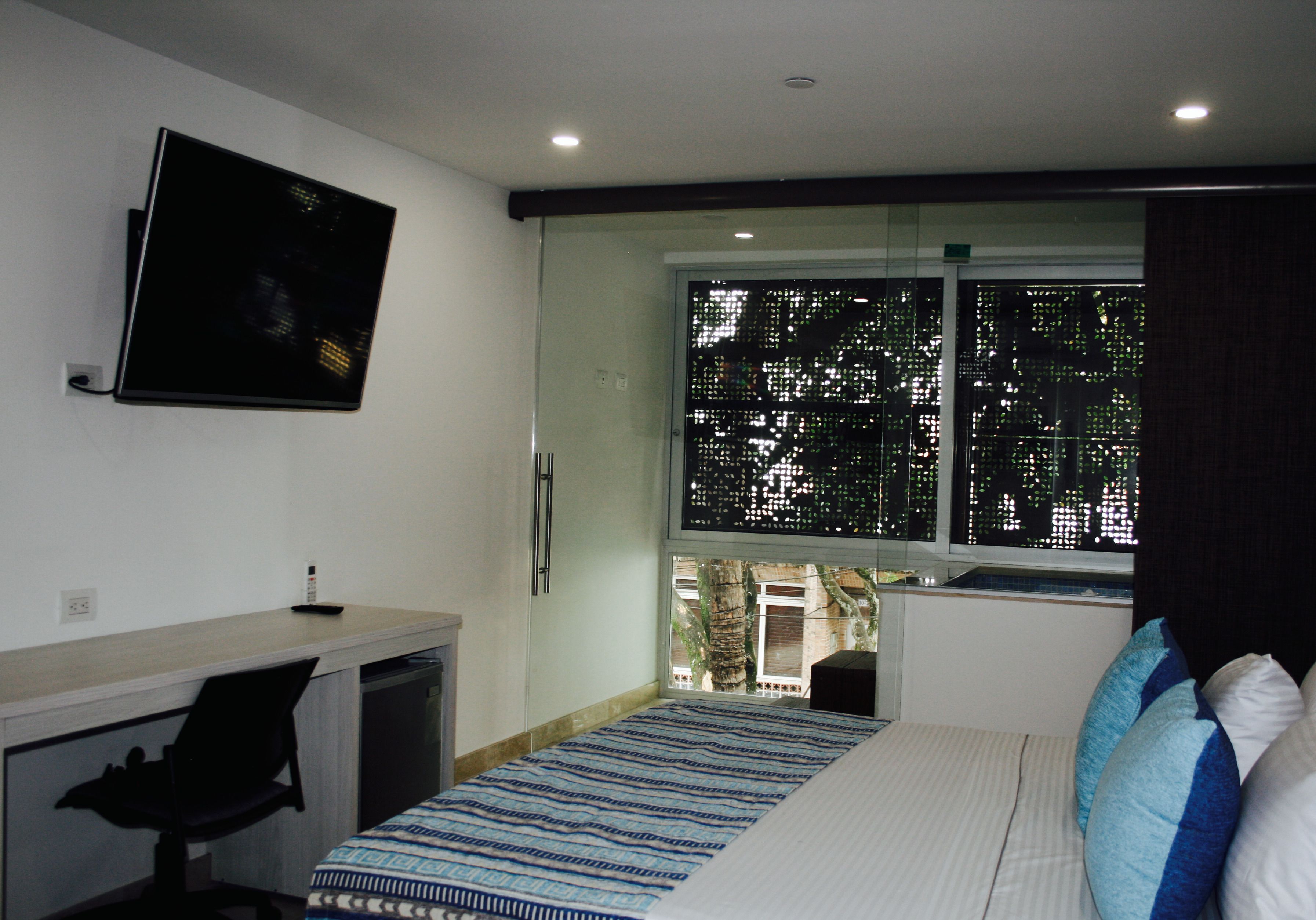 A bedroom with a bed, a desk, and a TV mounted on the wall.