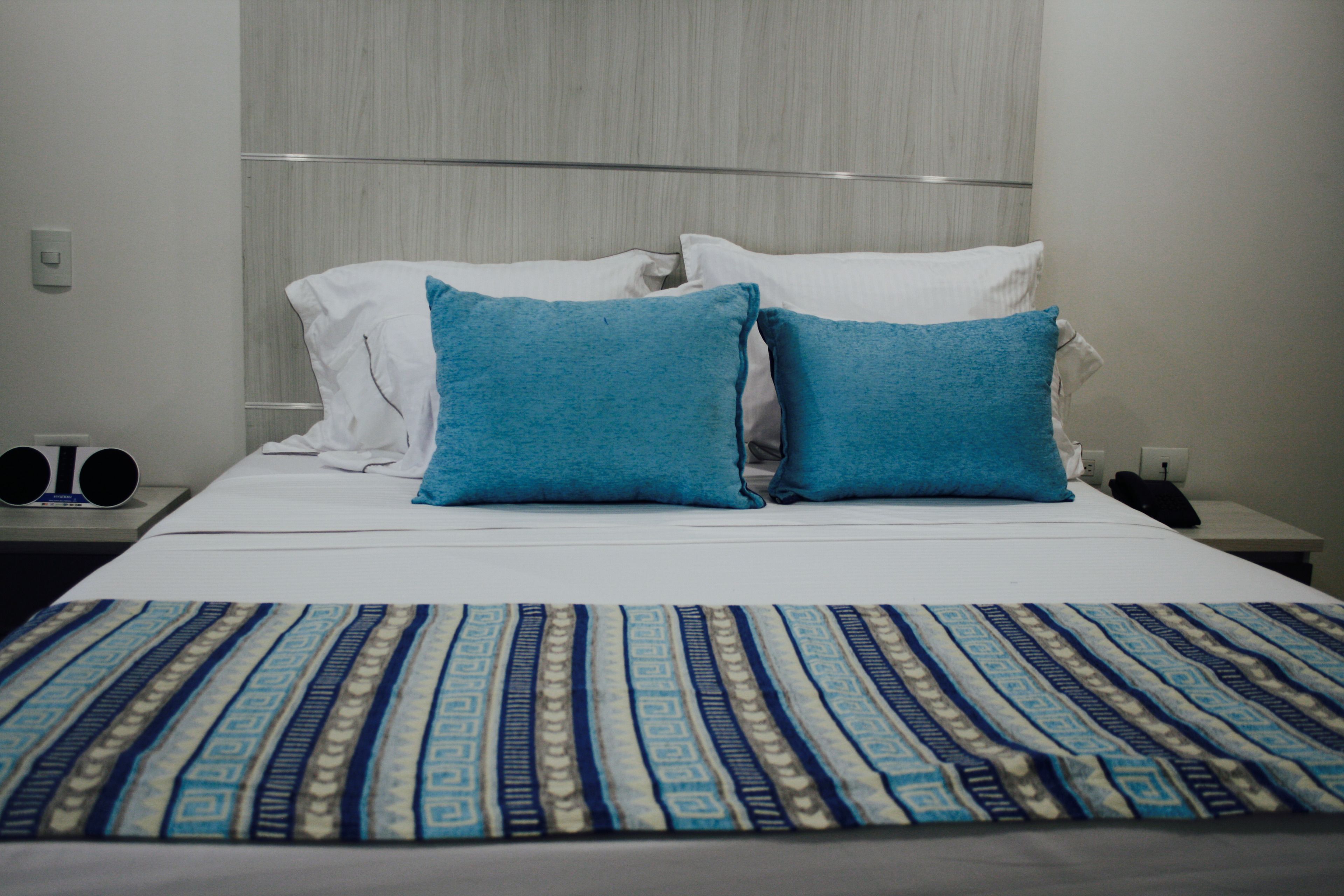 Habitación de hotel con cama, dos almohadas, mesita de noche, teléfono y radio.