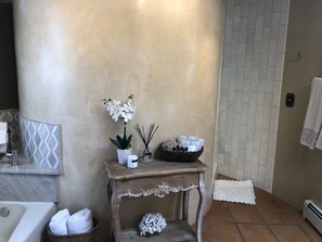 Une salle de bain avec un lavabo en marbre, un meuble-lavabo en bois agrémenté d’une orchidée blanche, un diffuseur de parfum à bâtonnets et un panier contenant des articles de toilette.