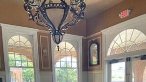 Comedor con candelabro, mesas, sillas y ventanas amplias con arcos.
