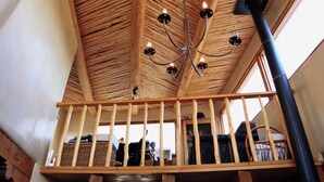 Techo de madera con candelabro, barandilla de balcón y un tubo negro.