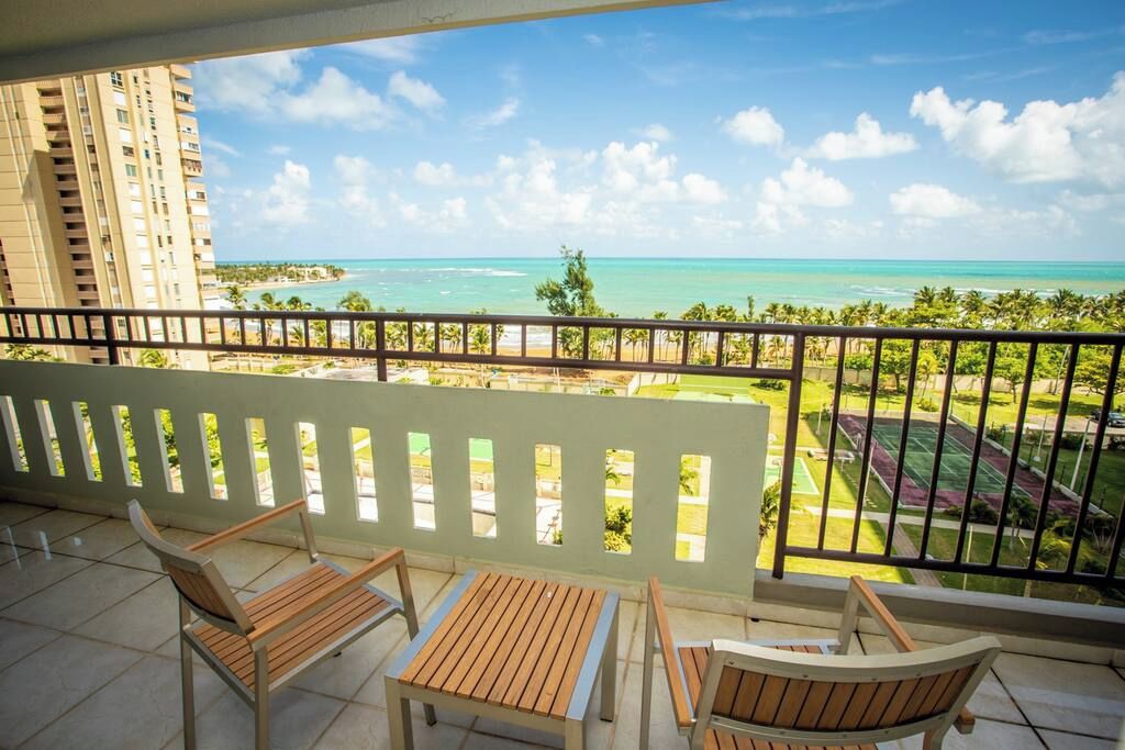 A balcony with wooden furniture and a view of the ocean and a golf course.