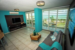A living room with a TV, sofa, and a view of the ocean. - ENCHANTED Jewel @ Playa Azul Luquillo Beach 9th Floor (Luquillo)