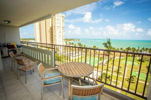 A balcony with a view of the ocean, a round wooden table, and several chairs.