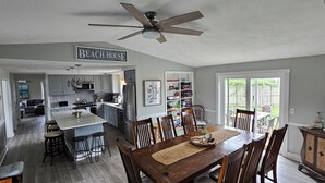 A spacious kitchen with a central island, a dining area with a wooden table and chairs, and a ceiling fan.