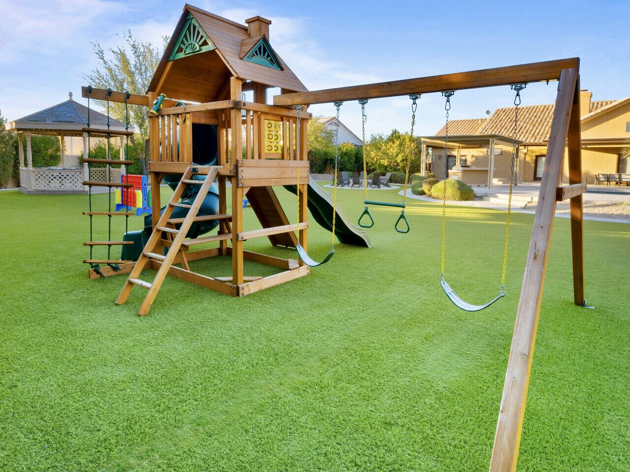 A wooden play structure with a slide and swings, set on artificial grass.