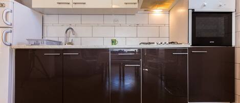 Een koelkast, een oven, een kookplaat, kookgerei, borden en bestek