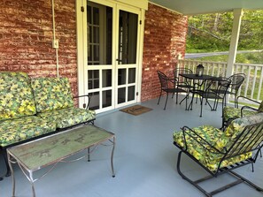 A covered porch with a brick wall, a sliding glass door, a table, and two patterned sofas. - The Tannery! Private Dipping Pool In The Warm Springs Stream! Pet Friendly! (Warm Springs)