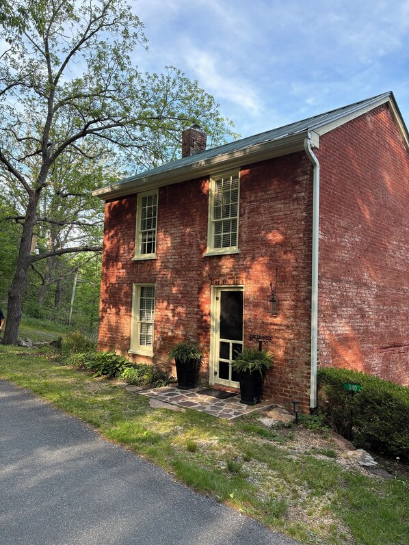 A brick building with two windows and a door, surrounded by greenery and a paved driveway. - The Tannery! Private Dipping Pool In The Warm Springs Stream! Pet Friendly! (Warm Springs)