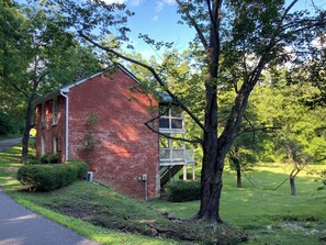A red brick building with a white balcony, surrounded by lush greenery and trees. - The Tannery! Private Dipping Pool In The Warm Springs Stream! Pet Friendly! (Warm Springs)