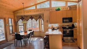 A wooden interior with a dining area, kitchen, and large windows.