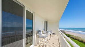 Ein Balkon mit Blick auf den Strand, weißen Geländern und gestreiften Stühlen.