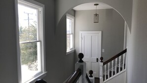 A hallway with a staircase, white door, and a hanging light fixture. - Serene Sauna Retreat with Chefs Kitchen, Luxury Beds & Luxury Baths (West Point)