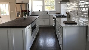 A modern kitchen with white cabinets, a wooden countertop, a stainless steel stove, and a window providing natural light. - Serene Sauna Retreat with Chefs Kitchen, Luxury Beds & Luxury Baths (West Point)