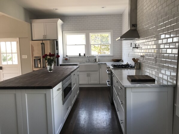A modern kitchen with white cabinets, a wooden countertop, a stainless steel stove, and a window providing natural light. - Serene Sauna Retreat with Chefs Kitchen, Luxury Beds & Luxury Baths (West Point)