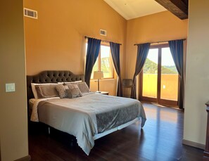 A large bedroom with a bed, a chair, and a view of the outdoors through a window. - Private Vineyard Estate Overlooking Pacific Ocean (Malibu)