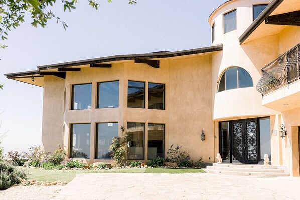 A modern two-story house with large windows, a curved roof, and a well-maintained garden. - Private Vineyard Estate Overlooking Pacific Ocean (Malibu)