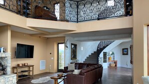 A spacious living area with a brown leather sofa, a stone fireplace, and a staircase with ornate railings. - Private Vineyard Estate Overlooking Pacific Ocean (Malibu)