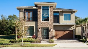 A modern two-story house with a stone facade, large windows, and a garage. - Luxury Cinderella Castle Villa in Reunion (Kissimmee)