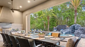An outdoor dining area with a view of a pool and waterfall, surrounded by lush greenery. - Luxury Cinderella Castle Villa in Reunion (Kissimmee)