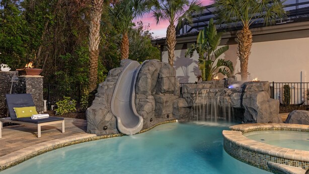 A pool with a water slide, lounge chairs, and palm trees. - Luxury Cinderella Castle Villa in Reunion (Kissimmee)