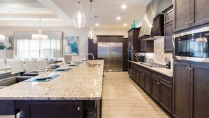 A modern kitchen with dark wood cabinets, stainless steel appliances, and a granite countertop. - Luxury Cinderella Castle Villa in Reunion (Kissimmee)