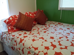 A bed with a red and white polka dot bedspread, two brown pillows, and a white pillow.